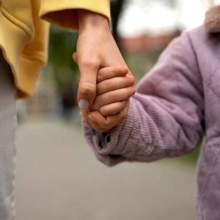 An adult holding a child's hand, symbolizing trust, care, and support in foster care.