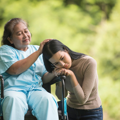 Elderly woman in a wheelchair sharing a comforting moment with a younger woman outdoors, promoting disability inclusion and caregiving support.