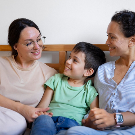 A happy child sitting between two adults, symbolising the warmth and connection in foster care or adoption in NSW.