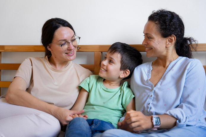 A happy child sitting between two adults, symbolising the warmth and connection in foster care or adoption in NSW.