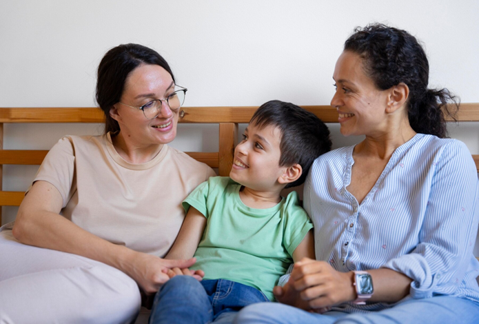 A happy child sitting between two adults, symbolising the warmth and connection in foster care or adoption in NSW.